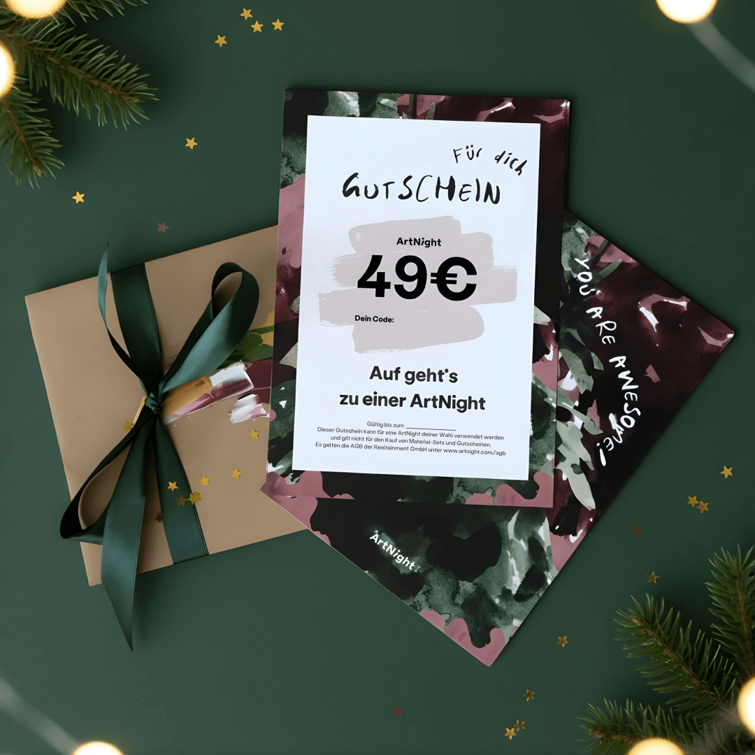 ArtNight Premium Gutscheine Geschenkkarte für eine ArtNight im Wert von 49 €, platziert auf einer grünen Fläche mit einem verpackten Geschenk und Tannenzweigen.