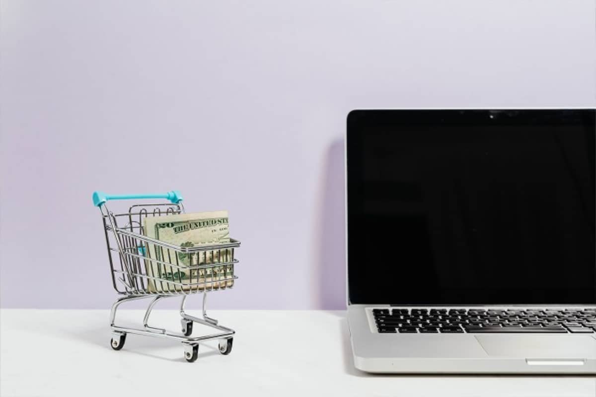 Ein Einkaufswagen mit Geld steht neben einem Laptop