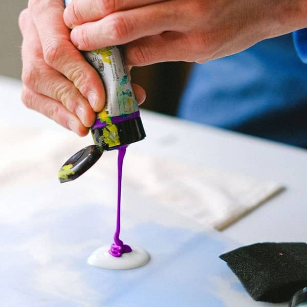 eine Lila Farbtube wird über weißer Farbe ausgedrückt.