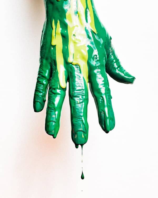 Hand mit tropfender grüner Farbe