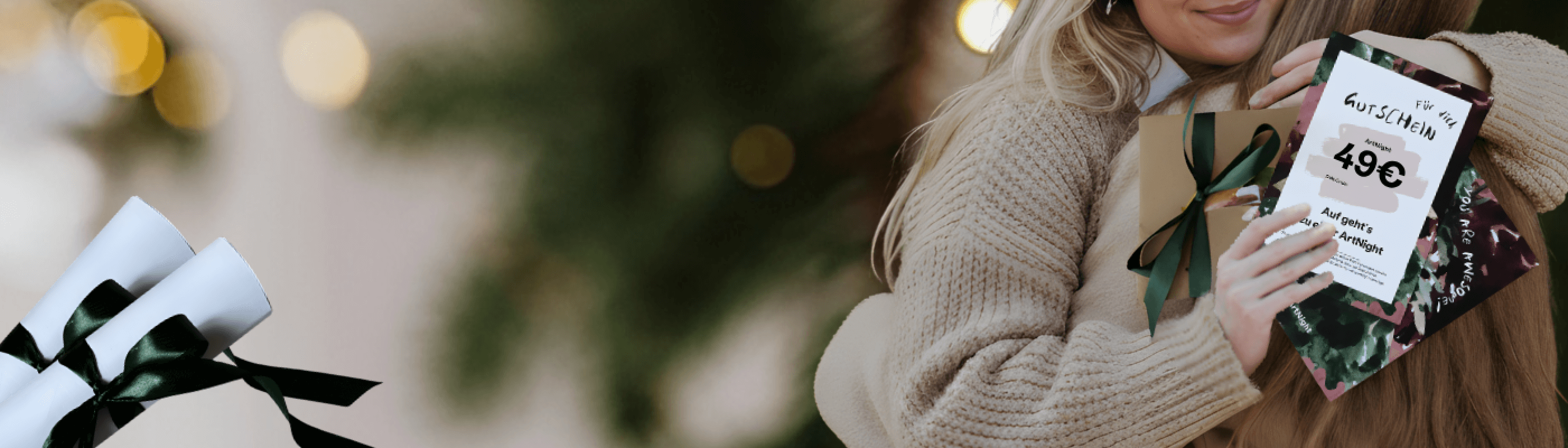 ArtNight Weihnachen 2025 Zwei Frauen umarmen sich neben einem Weihnachtsbaum und halten eine Geschenkkarte und verpackte Geschenke mit grünen Schleifen in den Händen.